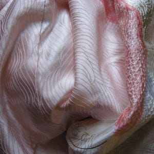 May include: A pink silk fabric with a wavy pattern. The fabric is folded and draped, showing the texture and sheen of the material.