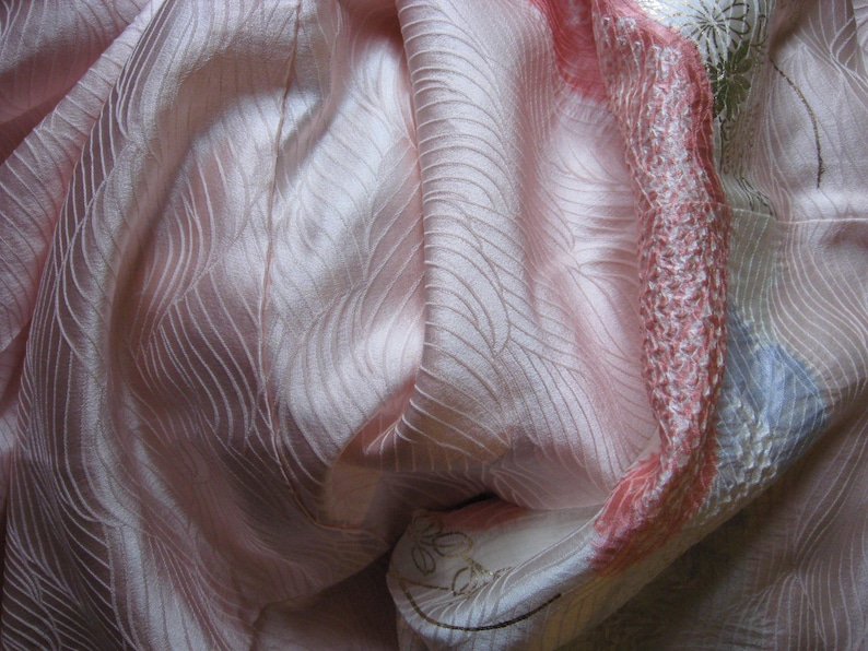 May include: A pink silk fabric with a wavy pattern. The fabric is folded and draped, showing the texture and sheen of the material.