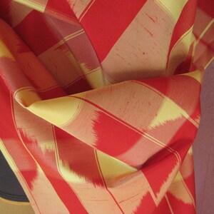 May include: Red and yellow striped fabric with a woven pattern. The fabric is folded and draped over a surface.