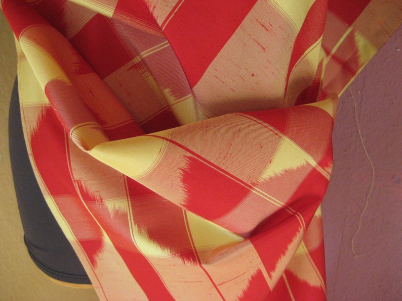 May include: Red and yellow striped fabric with a woven pattern. The fabric is folded and draped over a surface.