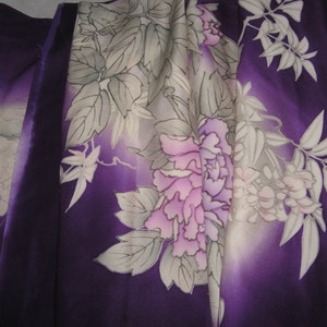 May include: A close-up of a fabric with a floral pattern. The fabric features large, stylized flowers in shades of pink and purple, with white and gray leaves. The background has a gradient of purple hues.