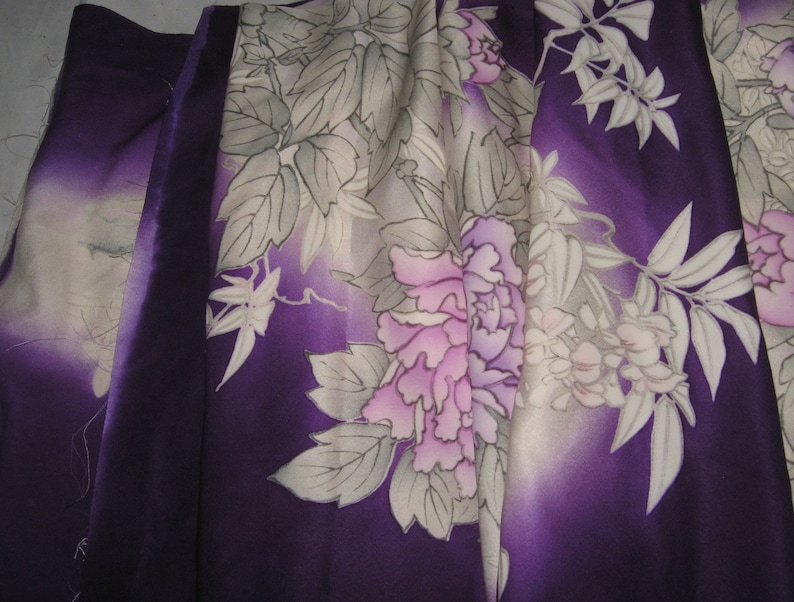May include: A close-up of a fabric with a floral pattern. The fabric features large, stylized flowers in shades of pink and purple, with white and gray leaves. The background has a gradient of purple hues.
