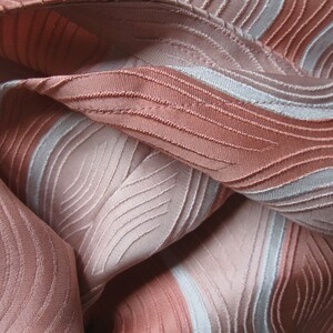 May include: A fabric featuring a textured, wavy pattern in shades of dusty rose and light silver. The material displays a series of raised, stitched lines that create a rhythmic, flowing design across the surface, with alternating bands of color.