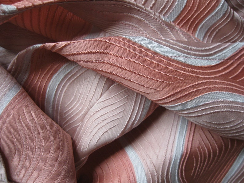 May include: A fabric featuring a textured, wavy pattern in shades of dusty rose and light silver. The material displays a series of raised, stitched lines that create a rhythmic, flowing design across the surface, with alternating bands of color.