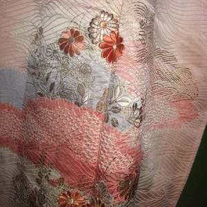 May include: A pink and white kimono with a floral pattern. The flowers are embroidered in gold, silver, and pink thread. The kimono is made of a soft, silky fabric.