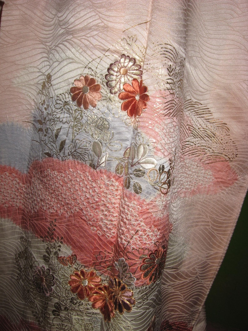 May include: A pink and white kimono with a floral pattern. The flowers are embroidered in gold, silver, and pink thread. The kimono is made of a soft, silky fabric.