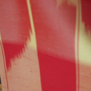 May include: A close-up of a red and cream striped fabric. The fabric has a subtle, textured pattern.