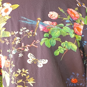 Könnte beinhalten: Dunkelmarineblaue Jacke mit Blumen- und Insektenmuster. Das Design zeigt rosa Rosen, weiße Schmetterlinge, blaue Libellen und einen roten Marienkäfer. Die Jacke hat einen hohen Kragen und einen detaillierten botanischen Druck.
