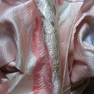 May include: A pink and white silk fabric with a gold floral pattern. The fabric is folded and draped, showing the texture and sheen of the material.