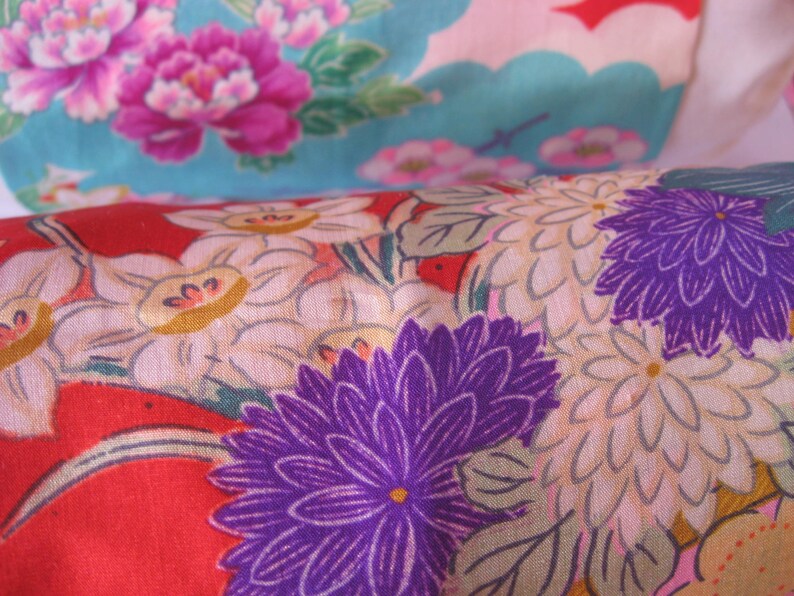 May include: Red fabric with a floral pattern featuring white, purple, and yellow flowers. The fabric has a textured surface.