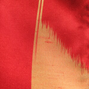 May include: Close-up of a red fabric with a gold vertical stripe pattern. The fabric has a woven texture.