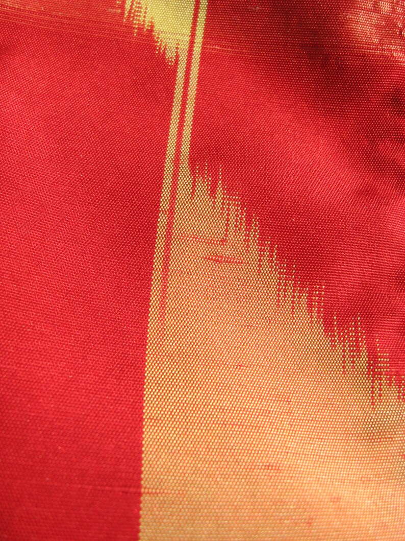 May include: Close-up of a red fabric with a gold vertical stripe pattern. The fabric has a woven texture.
