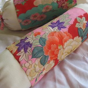May include: Two decorative pillows with a white fabric exterior and a floral patterned fabric interior. One pillow has a pink, red, and green floral pattern, and the other has a pink, red, and purple floral pattern.