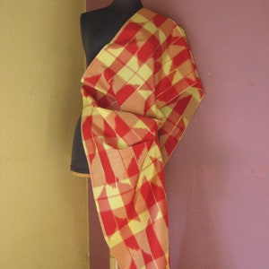 May include: A red and yellow plaid fabric draped over a dress form. The fabric has a geometric pattern with a subtle sheen.