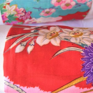 May include: Close-up of a red fabric with a floral pattern. The fabric features white, pink, and purple flowers with green leaves. The fabric is likely intended for quilting or crafting.