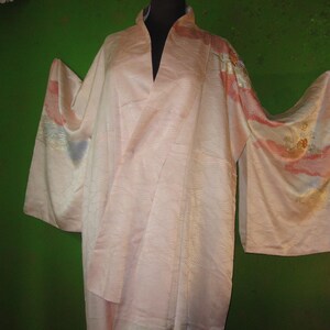 May include: A pale pink kimono with a V-neck and long sleeves. The kimono has a subtle floral pattern in shades of pink, blue, and gold.