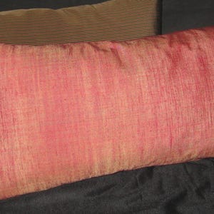 May include: Two rectangular throw pillows. The front pillow is a vibrant red with a textured appearance. The second pillow is a muted brown with a ribbed design. Both pillows are on a dark surface.