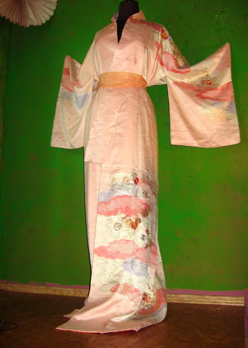 Könnte beinhalten: Ein rosafarbenes Seidenkimono mit Blumenmuster und einer goldenen Schärpe. Das Kimono wird auf einer Schaufensterpuppe vor einem grünen Hintergrund getragen.