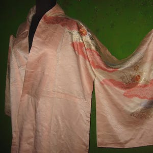 May include: A pink silk kimono with floral embroidery. The kimono has a long, flowing sleeve and a wide collar. The fabric is soft and delicate, and the embroidery is intricate and beautiful.