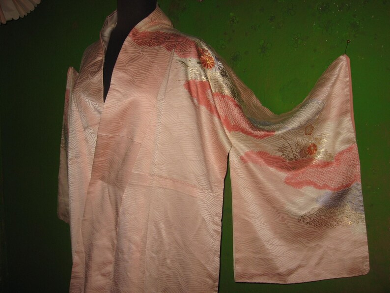 May include: A pink silk kimono with floral embroidery. The kimono has a long, flowing sleeve and a wide collar. The fabric is soft and delicate, and the embroidery is intricate and beautiful.