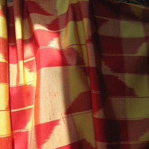 May include: Red and yellow striped fabric with a woven pattern. The fabric is folded and draped, creating a textured look.