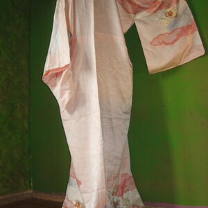 May include: A pink silk kimono with floral embroidery. The kimono has a long, flowing silhouette and is decorated with delicate floral patterns in shades of pink, white, and gold.