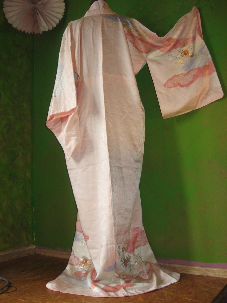 May include: A pink silk kimono with floral embroidery. The kimono has a long, flowing silhouette and is decorated with delicate floral patterns in shades of pink, white, and gold.