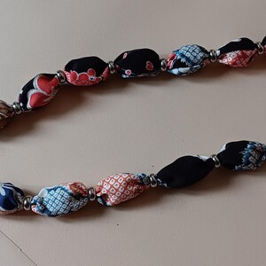 May include: Two decorative bag straps featuring a series of fabric-covered beads in black, red, white, and blue with floral and geometric patterns. Each bead is separated by small silver-toned metal spacers, and the ends feature silver metal rings.