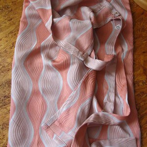 May include: A fabric piece featuring a textured, wavy pattern in shades of coral pink and light gray. The material has a distinct ribbed surface with vertical, undulating lines that create a sense of movement across the entire surface of the textile.