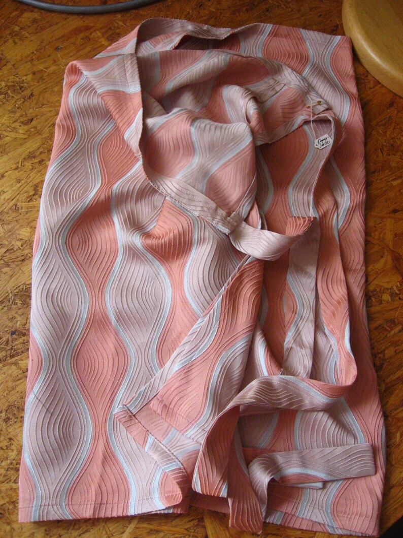 May include: A fabric piece featuring a textured, wavy pattern in shades of coral pink and light gray. The material has a distinct ribbed surface with vertical, undulating lines that create a sense of movement across the entire surface of the textile.