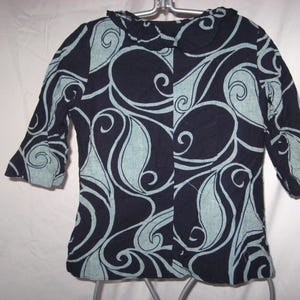 Può includere: Giacca blu navy con un motivo a vortice blu chiaro. La giacca ha maniche a tre quarti e un colletto arrotondato. Il tessuto sembra leggero, adatto alle temperature più calde.