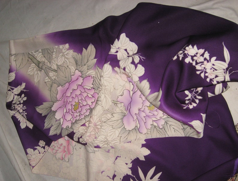 May include: A deep purple kimono with a floral design. The fabric features large, light pink peonies and white flowers with gray leaves. The kimono's design is a blend of traditional Japanese art and modern fashion.