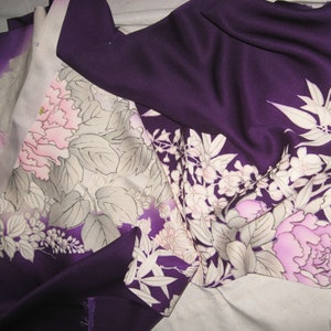 May include: Close-up of a folded fabric with a floral pattern. The fabric is primarily deep purple with a gradient to lighter shades. The floral design features pink and white flowers with gray leaves.