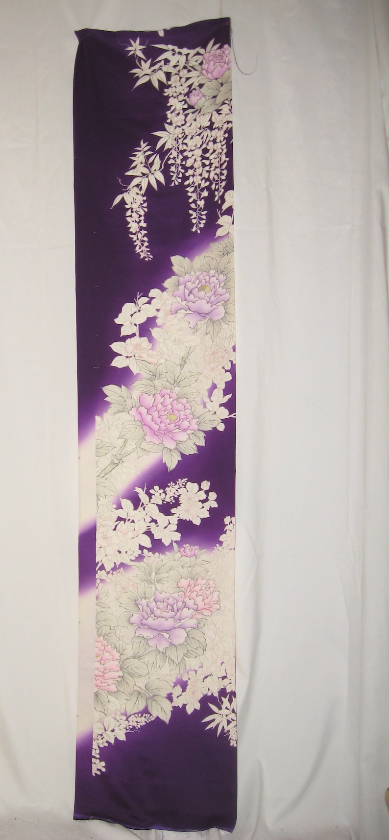 May include: A long, rectangular textile with a deep purple background and floral design. The design features large pink and lavender peonies, white wisteria, and other delicate white flowers and leaves. The fabric has a gradient effect.