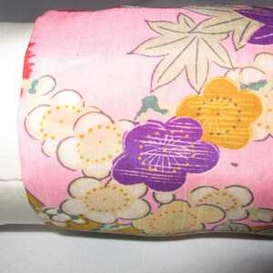 May include: Pink fabric with a floral pattern featuring purple, yellow, and white flowers. The fabric has a subtle sheen and a delicate texture.