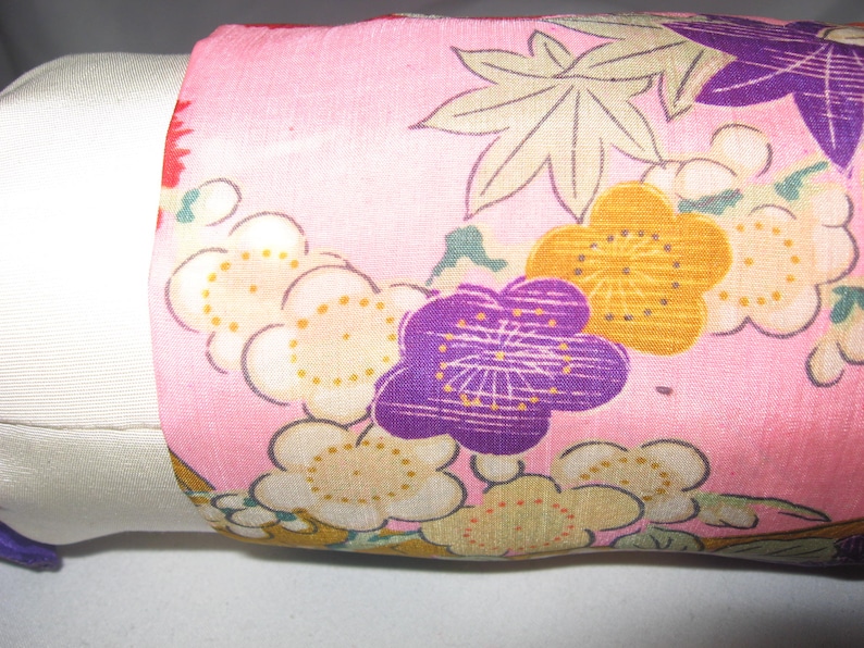 May include: Pink fabric with a floral pattern featuring purple, yellow, and white flowers. The fabric has a subtle sheen and a delicate texture.