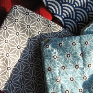 May include: A selection of patterned fabrics in a close-up shot. One features a grey geometric starburst design with black circles, another is light blue, and a third has a navy blue wave pattern. Suitable for crafts or home furnishings.