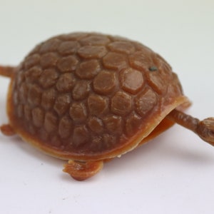 Pode incluir: Uma tartaruga de brinquedo de plástico marrom com uma casca detalhada e uma cabeça pequena. A tartaruga está em uma posição retraída com a cabeça e as pernas enfiadas dentro da casca.