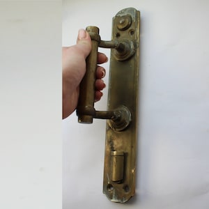 Puede incluir: Pomo de puerta antiguo de latón con una palanca y un pomo redondo. La manija está unida a una placa rectangular con detalles decorativos.