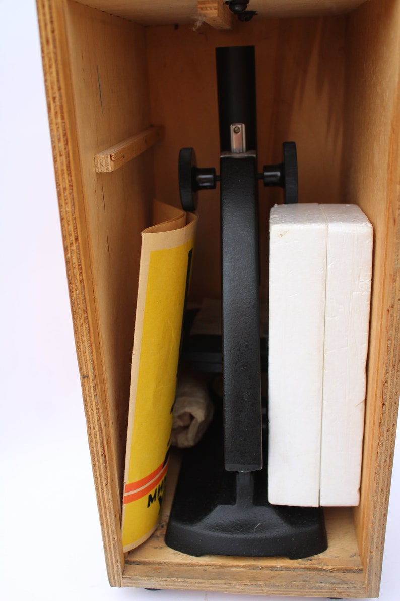 May include: A black microscope with a wooden storage case. The microscope has two knobs on the side and a white foam insert in the case.
