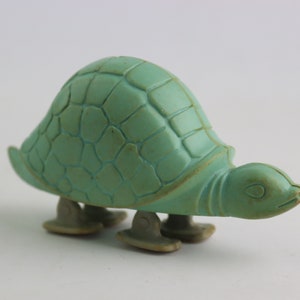 Op de afbeelding: Een groene plastic speelgoed schildpad met een gedetailleerde schild en vier wielen. De schildpad staat op een wit oppervlak.