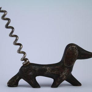 May include: A metal dachshund-shaped corkscrew with a silver corkscrew tail.