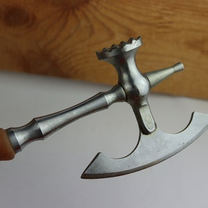 Könnte beinhalten: Ein silbernes und hölzernes Fleischklopfer-Werkzeug mit einem Hammerkopf, einem spitzen Ende und einer gebogenen Klinge. Der Griff ist hellbraun und das Werkzeug ist für den Küchengebrauch bestimmt.
