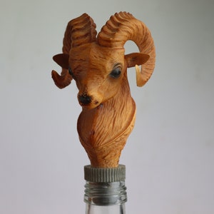 May include: A brown wooden bottle stopper shaped like a ram's head with large curled horns.