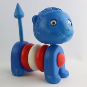 May include: A blue plastic toy lion with a red, white, and blue segmented body. The lion has a pointed tail and large white eyes.