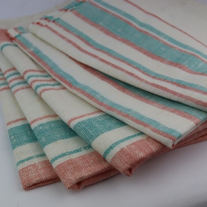 Puede incluir: Un montón de seis toallas de cocina blancas con rayas de color turquesa y coral. Las toallas están dobladas y apiladas.