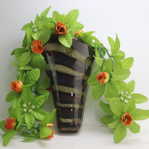 May include: A brown and black striped ceramic vase with a green leafy garland with orange flowers.
