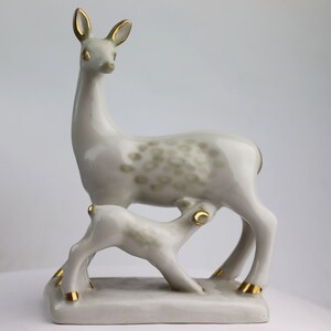 May include: A white porcelain figurine of a doe nursing her fawn. The doe has gold accents on her hooves and ears. The fawn is also white with gold accents on its hooves.