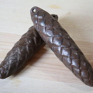 May include: Two brown metal pine cone shaped doorstops. The doorstops are textured and have a rustic look.