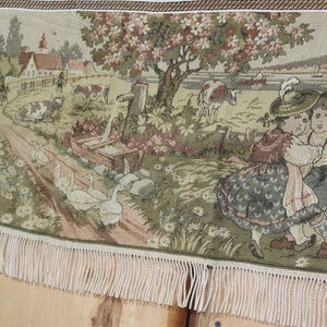 May include: A tapestry depicting a rural scene with a farmhouse, a tree in blossom, a well, a path, geese, cows, and two children in traditional dress. The tapestry has a fringed border.